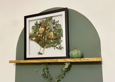 an arrangement of flowers is displayed on a shelf above a vase with leaves and pumpkins