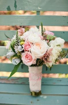 a white vase filled with pink and white flowers on top of a wooden table next to a blue wall