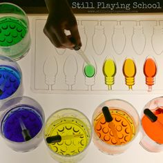 a child's hand is playing with different colored sand and water in plastic cups