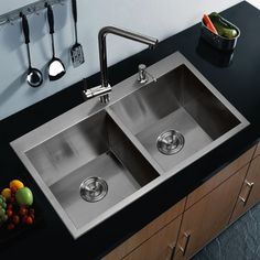 two stainless steel kitchen sinks with black counter tops and utensils hanging on the wall