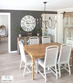 a dining room table with white chairs and a large clock on the wall behind it