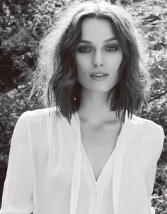 black and white photo of a woman with shoulder length hair wearing a white shirt in front of trees