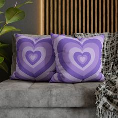 two purple heart pillows sitting on top of a couch next to a potted plant