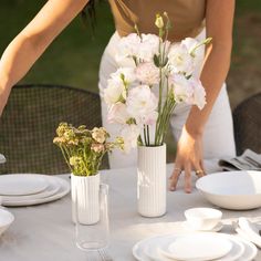 a woman placing flowers in vases on a table with plates and utensils