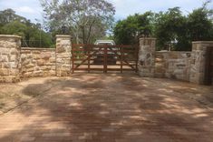 a brick driveway with a gate and stone walls