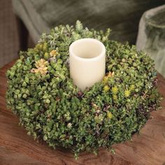 a white candle is sitting on top of a wooden table with greenery around it