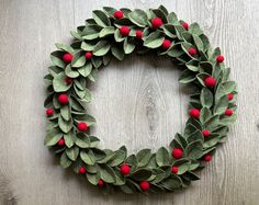 a wreath made out of leaves and red berries on a wooden surface with scissors next to it