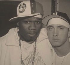 two young men are posing for the camera with one wearing a hat and the other in a white jacket