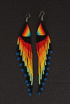 two pairs of earrings with multicolored wings on them, hanging from black background