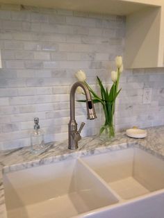 two white tulips in a glass vase on the kitchen counter top next to a double sink