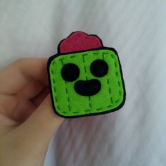 a hand holding a small green and red piece of felt with a face on it