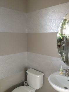 a white toilet sitting next to a sink in a bathroom under a large round mirror