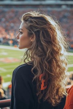 Woman with long wavy hair watching a football game in a stadium. Cute Game Day Hairstyles Football, Gameday Hairstyles Football College, Curly Hairstyles For Football Games, Hair Styles For Football Games, Game Day Hairstyles Soccer, Cheer Game Day Hair Football Season, Game Day Hairstyles Football College, Football Game Hair