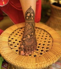 a woman's foot with henna tattoos on it sitting on a wicker chair