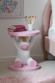 a pink and white pig shaped end table with books on it's head, holding pencils in its mouth