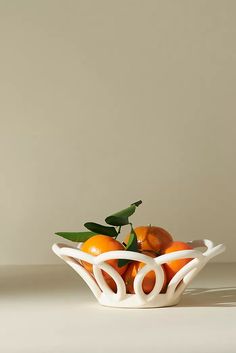 a white bowl filled with oranges on top of a table next to a wall