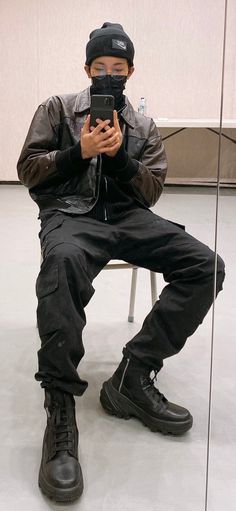 a man sitting on a chair while holding a cell phone in his hand and wearing a black hat