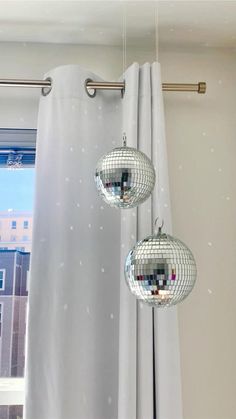 three disco ball lights hanging from a curtain in front of a window with buildings outside