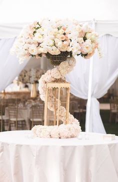 a birdcage filled with flowers sitting on top of a white table cloth covered table