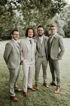 three men in suits standing next to each other on a grass covered field with trees behind them