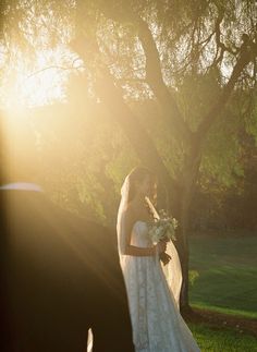 a bride and groom standing in front of a tree at their outdoor wedding ceremony with the sun shining on them