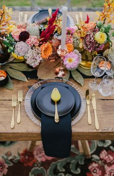 the table is set with black plates and gold utensils, yellow napkins, and colorful floral centerpieces