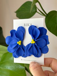 a pair of blue flower earrings sitting on top of a card next to a plant