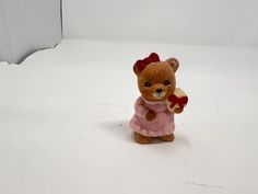 a teddy bear figurine with a heart in its hand on a white surface