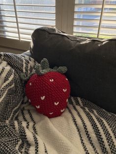 a red knitted strawberry sitting on top of a bed next to a black and white pillow