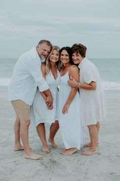 three women and two men standing together on the beach with their arms around each other