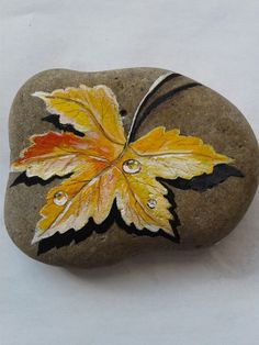 a leaf painted on top of a rock with water droplets in the middle and yellow leaves on it