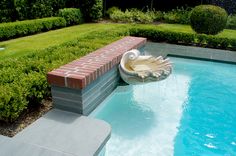 a pool with a fountain in the middle of it next to a lush green yard