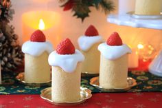 three small cakes with white icing and strawberries on top sitting on a table