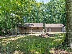 a house in the woods with trees and grass on the ground, surrounded by wooded area