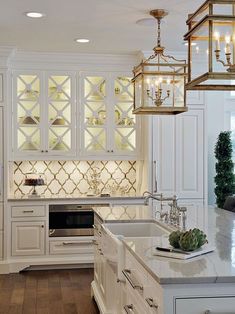 a kitchen with white cabinets and gold chandelier hanging from the ceiling over the sink