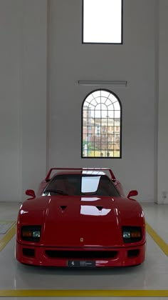 a red sports car is parked in an empty room with yellow lines on the floor