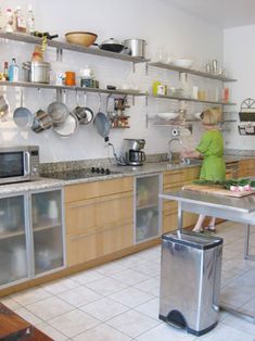 a woman standing in a kitchen next to a table with a trash can on it