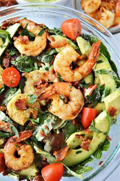 a salad with shrimp, avocado and tomatoes in a glass bowl on a table