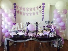 a table topped with lots of purple and white balloons next to a wall filled with cake