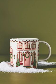 a coffee cup sitting on top of a table covered in white snow next to a green wall