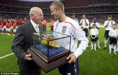 two men standing next to each other in front of a trophy on a soccer field