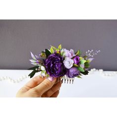 a hand holding a comb with purple flowers on it and greenery in the middle