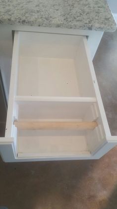 an open drawer in the middle of a kitchen counter with marble top and white cabinets