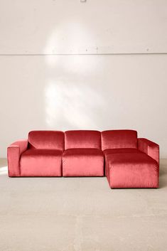 a red couch sitting on top of a floor next to a white wall in an empty room