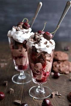 two glasses filled with ice cream and cherries on top of a wooden table next to cookies