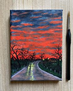 a painting of a road at sunset with trees in the background and a pen resting on top