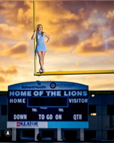 a woman standing on top of a yellow pole in front of a sign that reads home of the lions