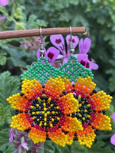 colorful beaded earrings hanging from a tree branch with flowers in the backgroud