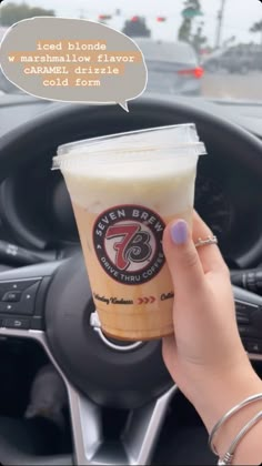 a woman holding up a cup of coffee in her car