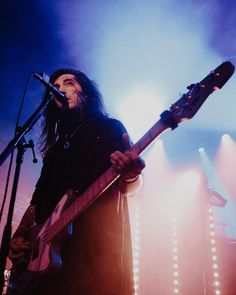 a man with long hair holding a guitar in front of a microphone and stage lights